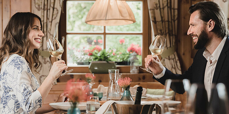 Zwei Gäste des Löwen Hotel Montafon trinken in einem Restaurant Weißwein und blicken sich an