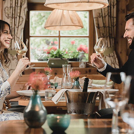 Zwei Gäste des Löwen Hotel Montafon trinken in einem Restaurant Weißwein und blicken sich an