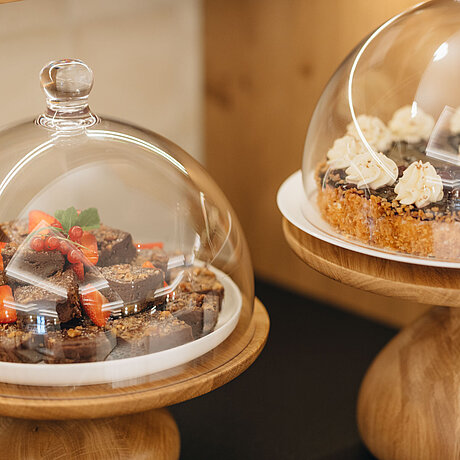 Zwei mit süßen Dessertstücken belegte Teller werden unter einer Glasglocke ausgestellt
