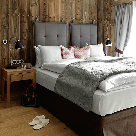 In einem Schlafzimmer des Löwen Hotel Montafon steht eine freistehende Badewanne sowie ein hohes Doppelbett mit dekorativen Kissen