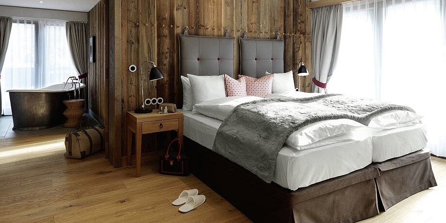 In einem Schlafzimmer des Löwen Hotel Montafon steht eine freistehende Badewanne sowie ein hohes Doppelbett mit dekorativen Kissen