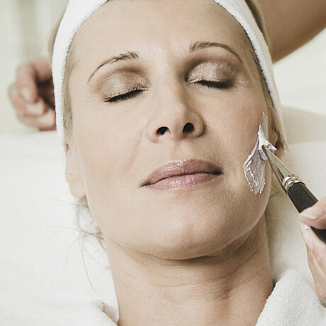Eine Mitarbeiterin führt bei einer entspannten Dame im Löwen Hotel Montafon eine Kosmetikbehandlung durch