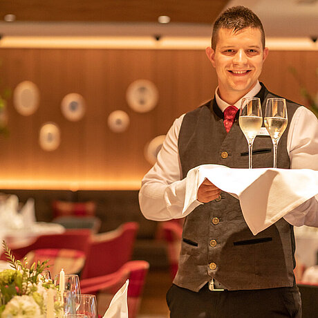 Ein Kellner des Löwen Hotel Montafon serviert Sekt in zwei hohen Gläsern