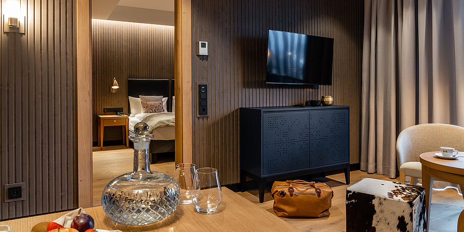 Living area of the Deluxe Room with flat screen TV, cosy sitting area and fine glass carafe on the dining table
