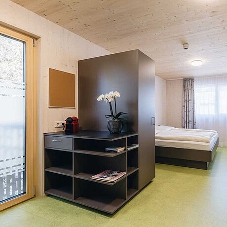 Innenaufnahme es Doppelzimmers mit Schrank, Bett und Regal im Löwen-Teamhaus