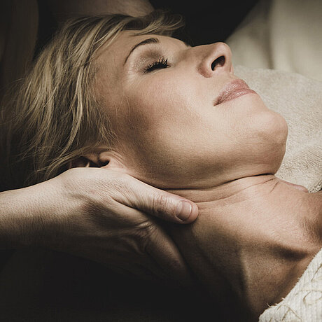 Ein Masseur stützt den Nacken einer Dame bei einer Massage