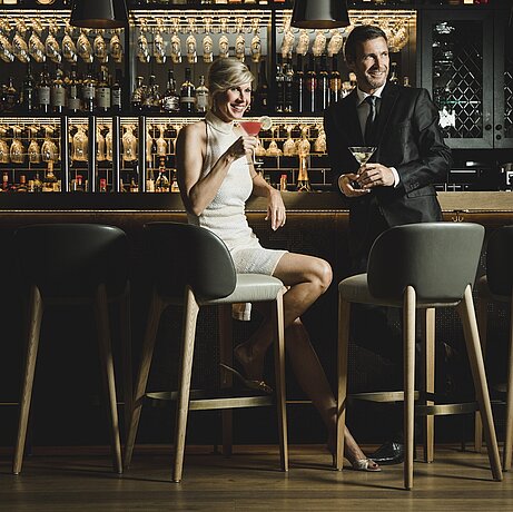 Ein junges Paar sitzt am Tresen der Bar im Löwen Hotel Montafon und genießt leckere Drinks