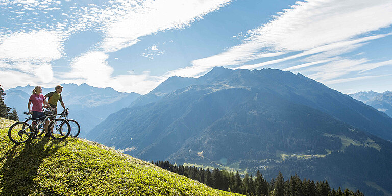 Two mountain bikers on the Bartholomaeberg look at the surrounding Montafon mountain panorama in Vorarlberg.