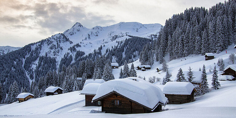 Mehrere Holzhütten im Gebirge von Vorarlberg sind von dicken Schneeschichten bedeckt