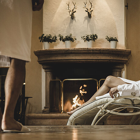 A woman lies in a lounger in front of a fireplace in the Löwen Hotel Montafon