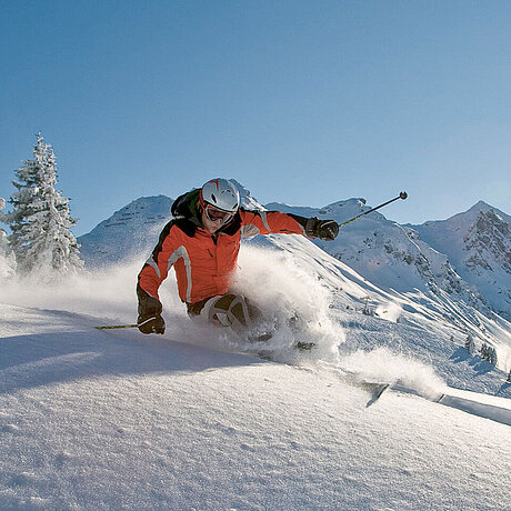 Ein Wintersportler fährt mit Skiern durch den frischen Schnee nahe des Löwen Hotel Montafon