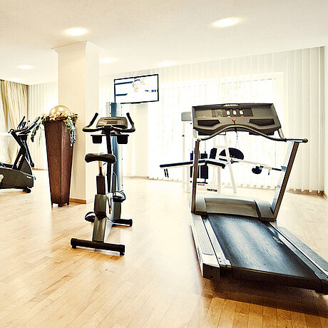 Ein Laufband und ein Heimtrainer stehen im Fitnessbereich des Wellnesshotels in Vorarlberg vor einem Fernseher